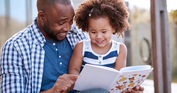 Father with young child reading a picture book outdoors