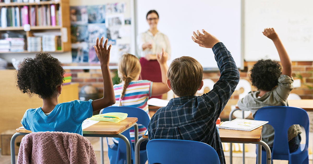 Students in an elementary school classroom with their hands raised