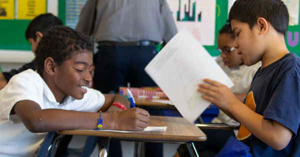 Photo of two kids working together at a desk.